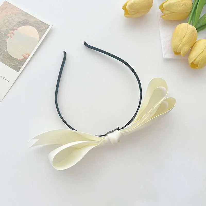 French satin bow headband for women featuring a delicate cream satin bow on a sleek black bow headband