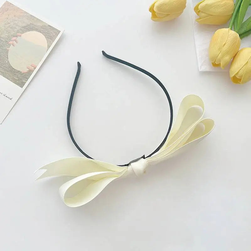 French satin bow headband for women featuring a delicate cream satin bow on a sleek black bow headband