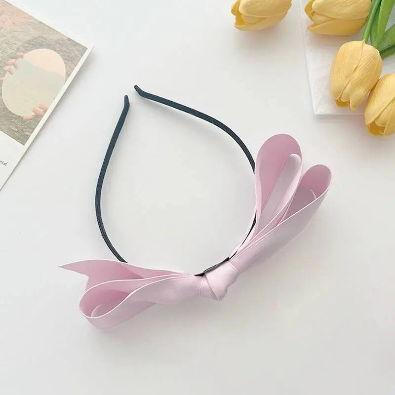 A delicate pink french satin bow adorns a sleek black satin bow headband for women