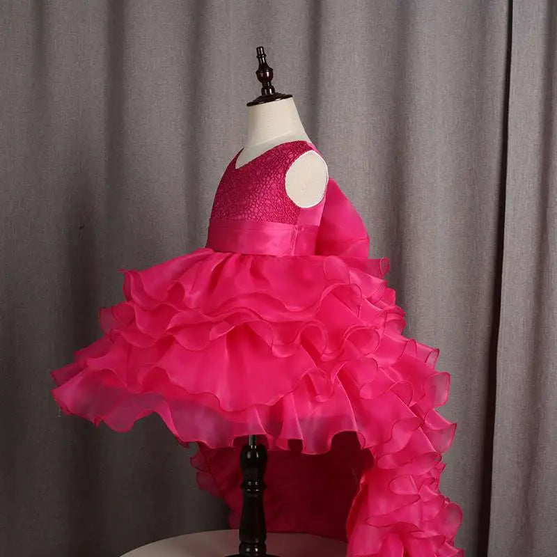 A vibrant fuchsia layered ruffled flower girl tuxedo dress with lace bodice and trailing skirt for special occasions