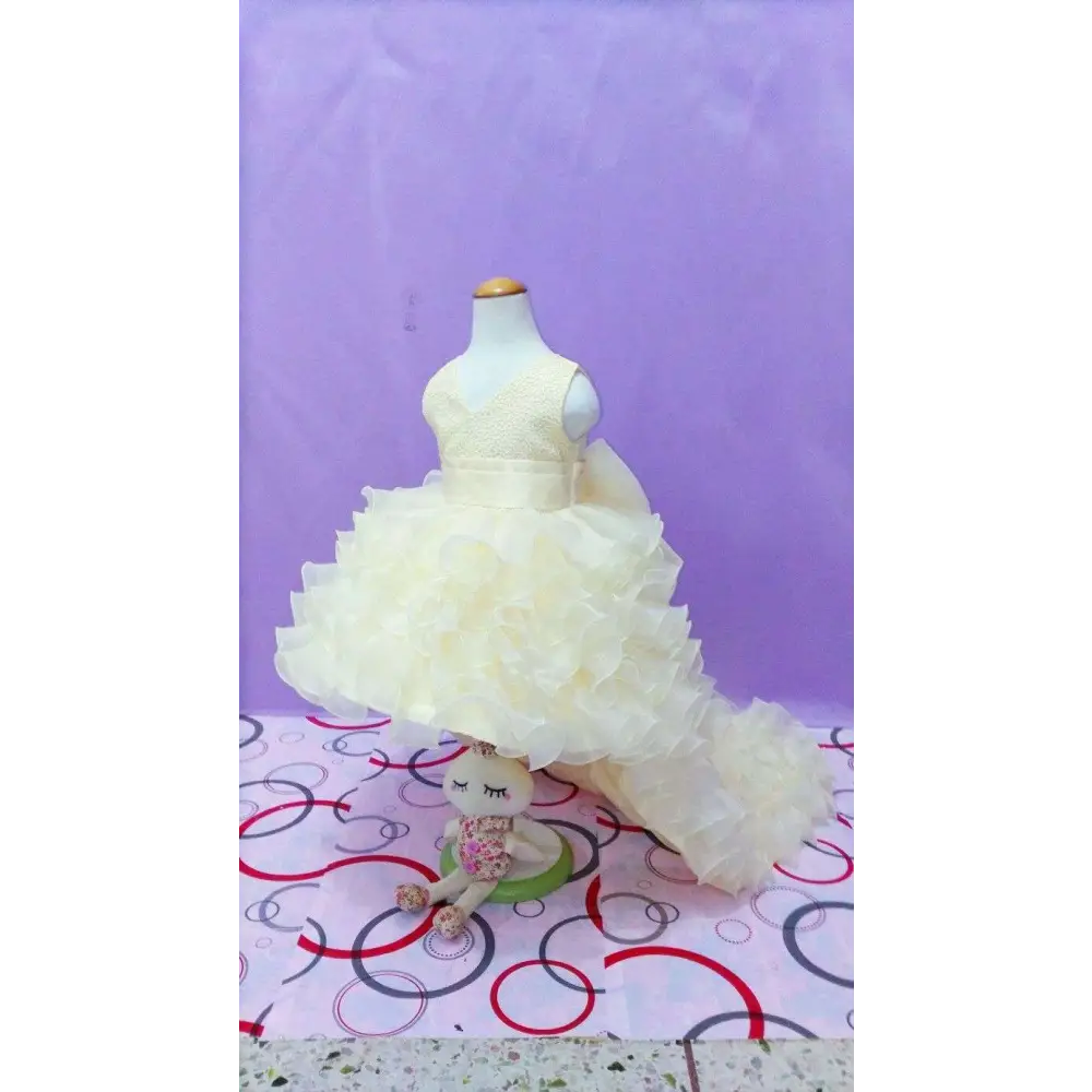 A delicate ivory ruffled flower girl tuxedo dress with fitted bodice and voluminous skirt on mannequin