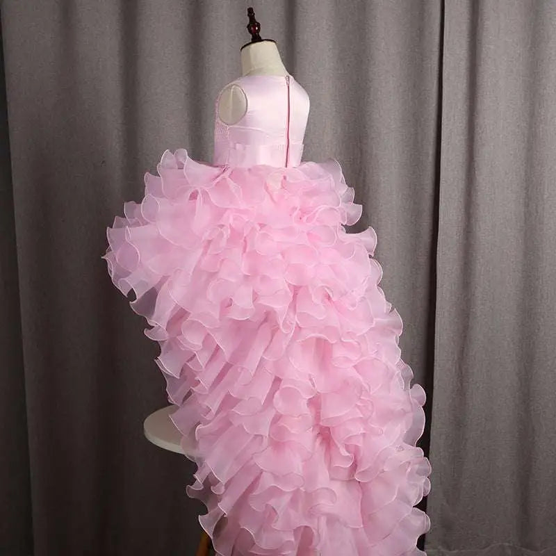 A delicate fuchsia layered ruffled flower girl tuxedo dress with satin bodice and trailing tulle skirt on a mannequin