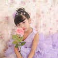 A young girl wears a fuchsia layered ruffled flower girl tuxedo dress holding a pink rose in lavender lace
