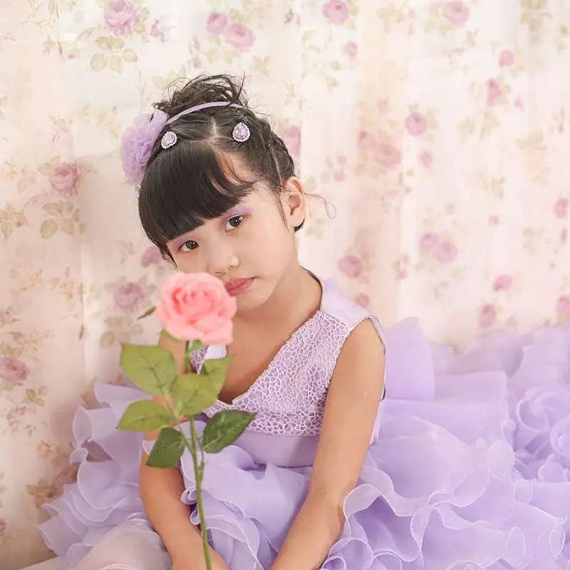 A young girl wears a fuchsia layered ruffled flower girl tuxedo dress holding a pink rose in lavender lace