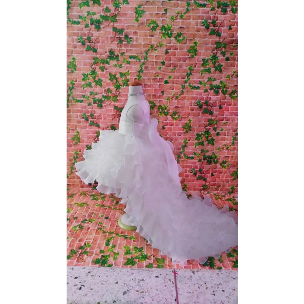 A white multi-layered ruffled wedding gown on a mannequin for a fuchsia layered ruffled flower girl tuxedo trailing dress