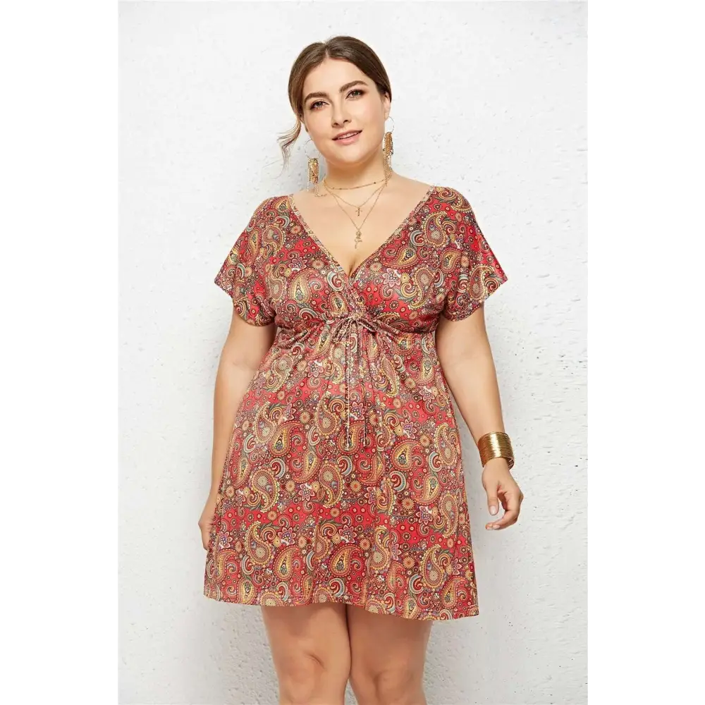 A plus-size woman wears a red and gold paisley printed deep v-neck elastic waist dress with flutter sleeves