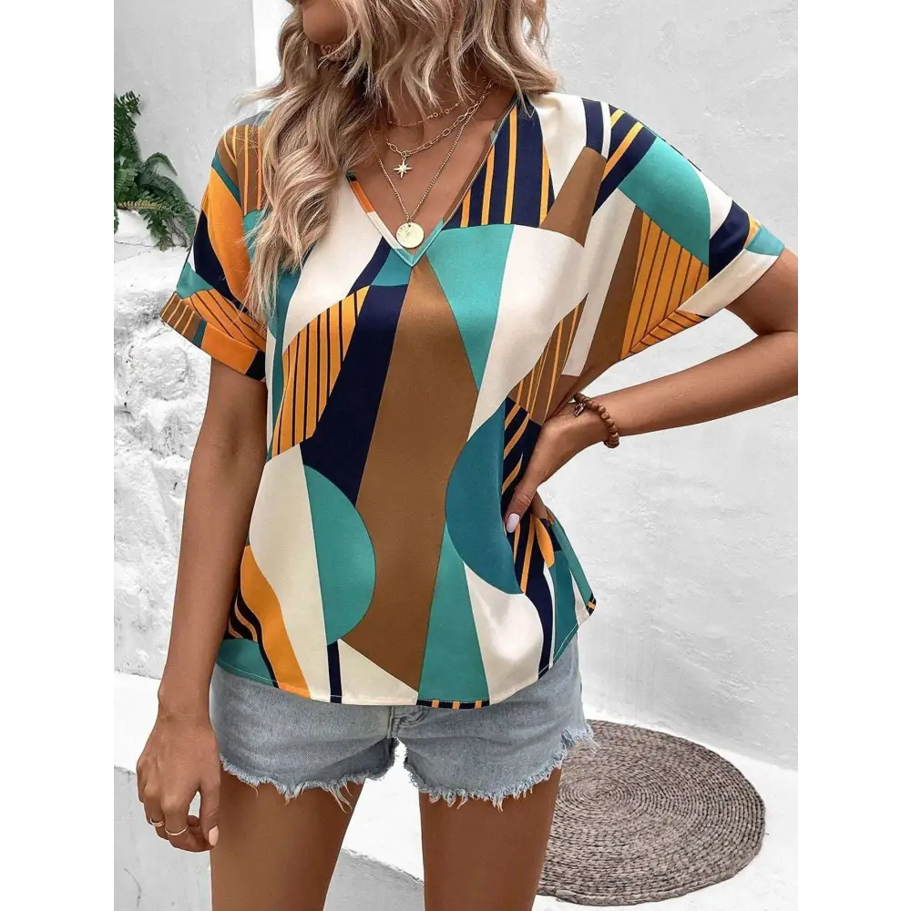 A woman wears a vibrant geometric-patterned women’s clothing printed v-neck top in teal orange navy blue and cream