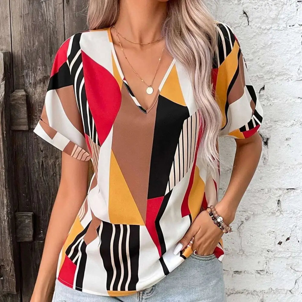 A vibrant geometric-patterned women’s printed v-neck top with bold red black yellow and white abstract shapes