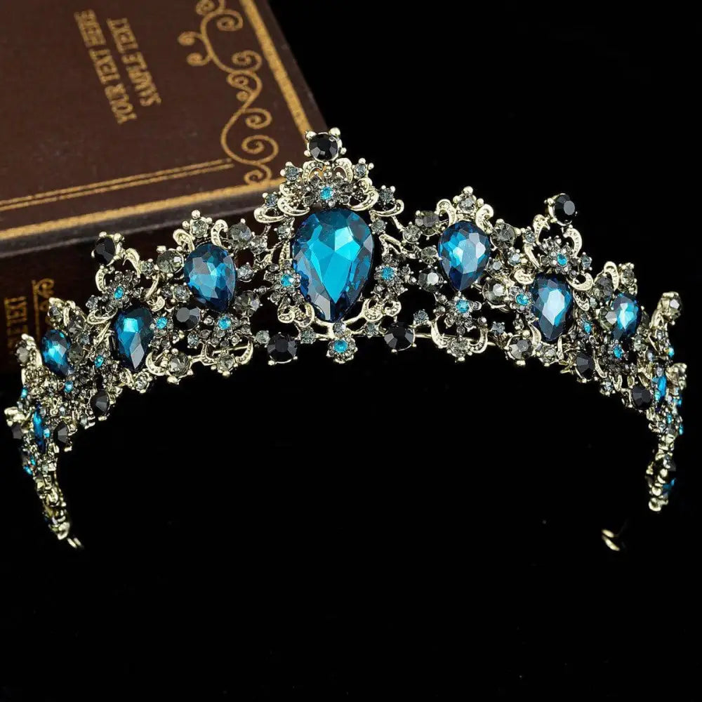 An ornate silver crystal bridal crown with large blue teardrop crystals and gold baroque rhinestone accents