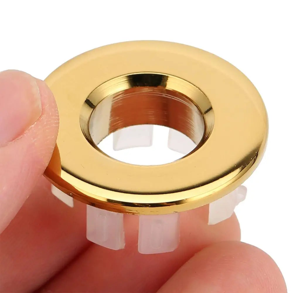 Gold bathroom wash basin sink hole overflow cover with gold-colored metallic ring and four translucent plastic tabs