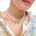 A delicate pearls necklace with lustrous white pearls and a gold bow pendant for luxury women’s fashion looks