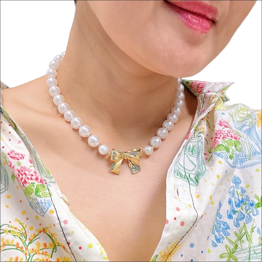 A delicate pearls necklace with lustrous white pearls and a gold bow pendant for luxury women’s fashion looks