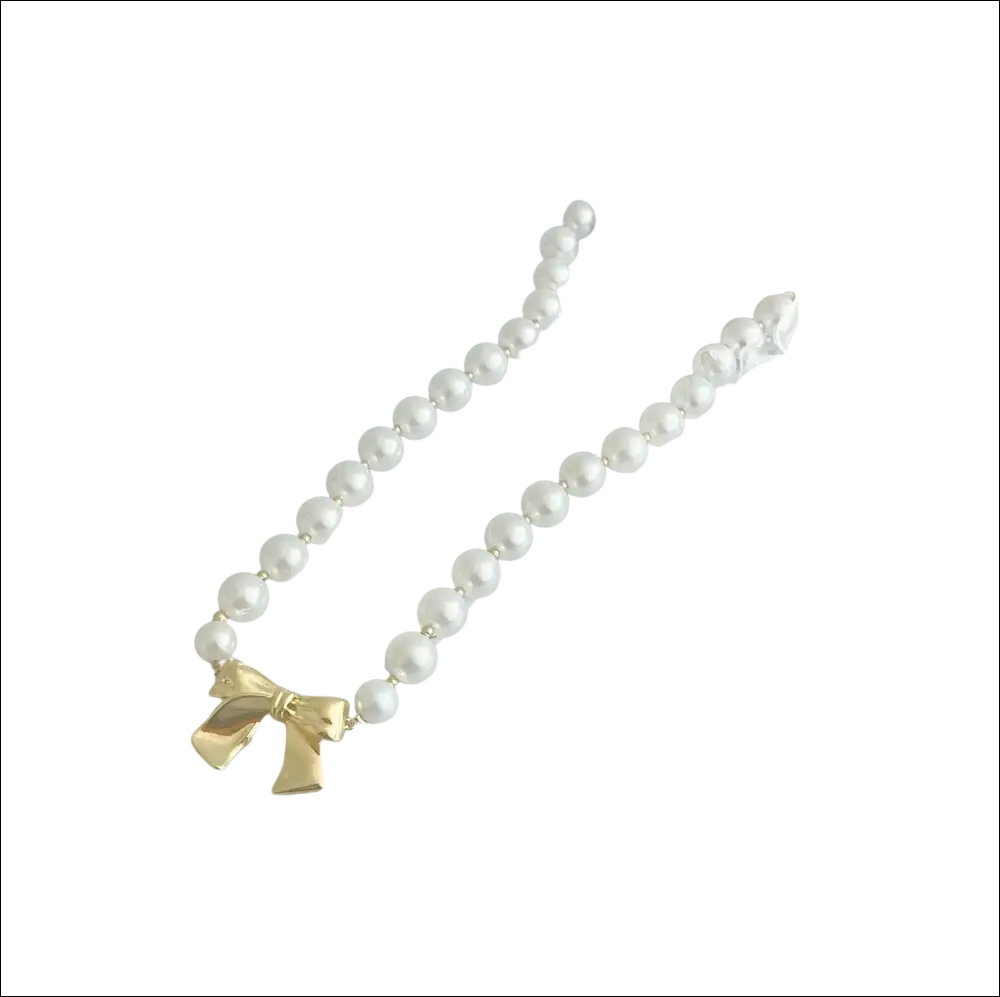 A delicate white pearls necklace with a gold bow charm in luxury women’s fashion packaging with a pink tag