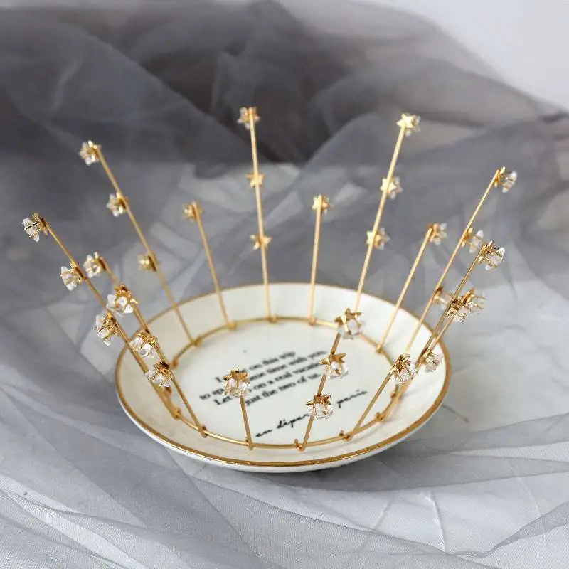 A delicate gold crystal bride handmade star crown with clear crystal flowers on a white ceramic dish