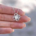 A silver-toned gold floral knot daughter’s love necklace with a central round-cut diamond and intricate swirling design