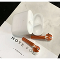 White and copper-colored apple airpods 2 with gold glossy custom sticker skin resting in matching charging case