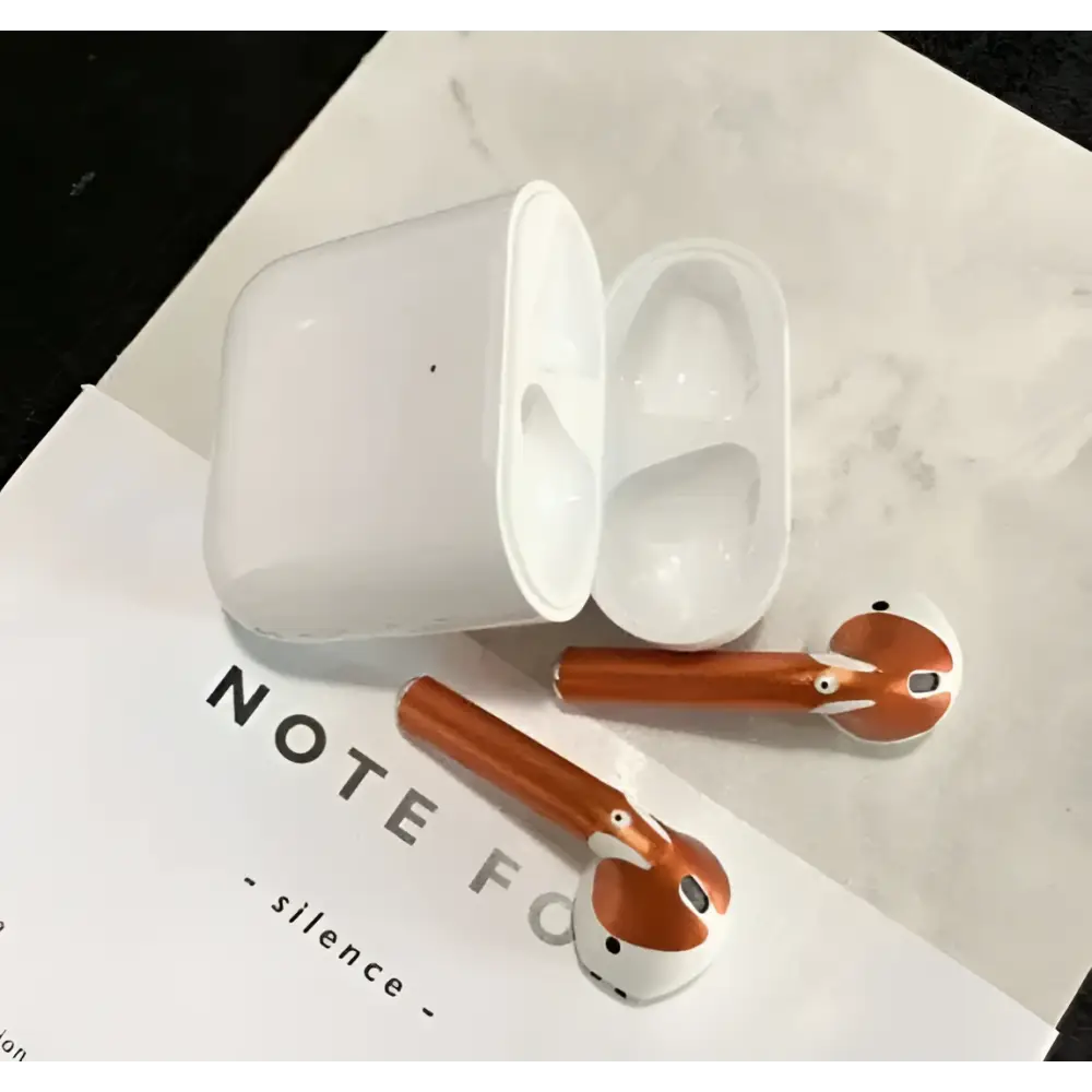 White and copper-colored apple airpods 2 with gold glossy custom sticker skin resting in matching charging case