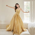 A shimmering gold satin heavy industry birthday dress with a fitted bodice and flowing pleated skirt