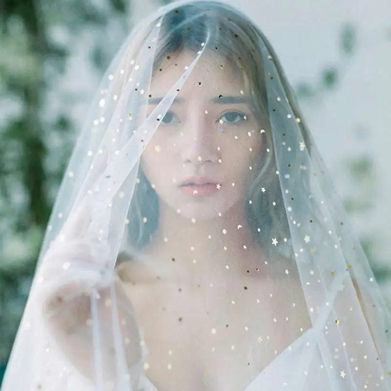 A golden shiny big veil in white sheer fabric adorned with star-shaped embellishments in gold and silver