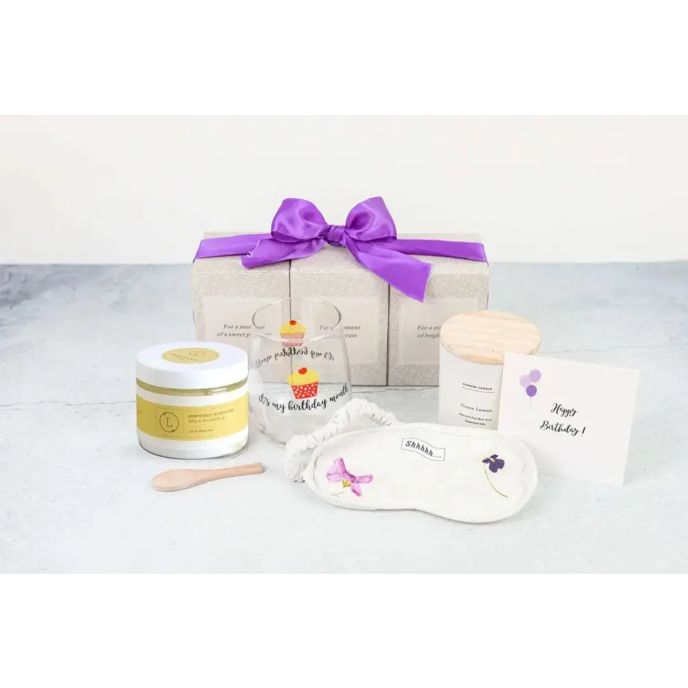 White embroidered eye mask with purple flower design included in grapefruit body scrub and wine glass spa gift basket