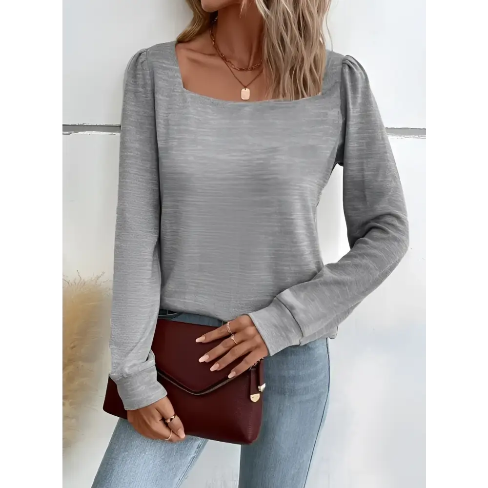 A maroon faux leather clutch with flap closure and gold-tone hardware paired with a gray solid color square neck versatile long sleeved top