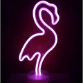 A glowing purple led neon lights sign shaped like a flamingo creating a perfect ambiance with green christmas tree decor