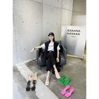 Black leather chair with sleek modern design and visible stitching displayed alongside green minimalist square toe block heel sandals