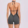 A sleek dark gray halter neck high yoga romper with v-cut neckline featuring a back tie and ruched detailing