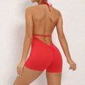 Red halter neck high yoga romper featuring form-fitting shorts with ruched back and tie-back straps, back view