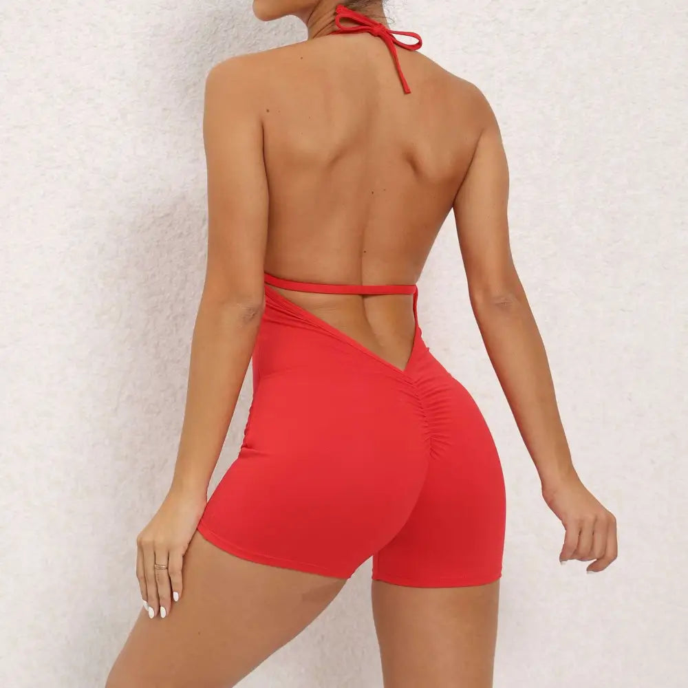 Red halter neck high yoga romper featuring form-fitting shorts with ruched back and tie-back straps, back view