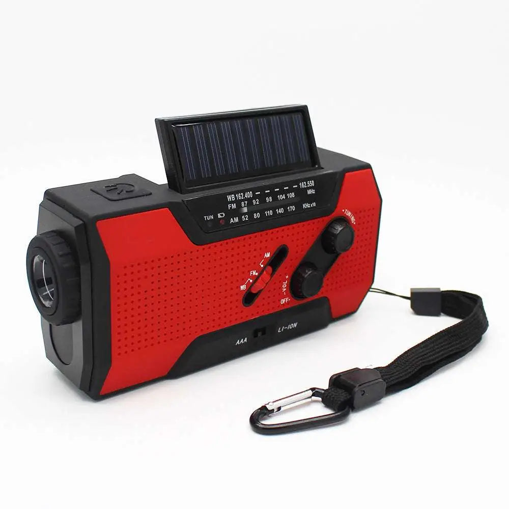 Red and black crank solar emergency radio with built-in flashlight, perforated speaker grille, and carabiner strap for portability