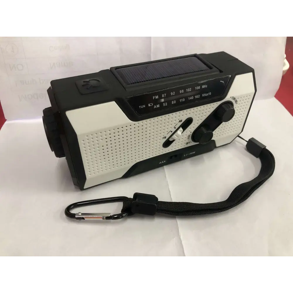 Black and white crank solar emergency radio with perforated panel, two rotary knobs, fm/am dial, and carrying strap