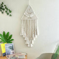 A cream-colored handwoven home decor triangle dream catcher with intricate knotwork and dream catcher tassels