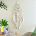 A cream-colored handwoven home decor triangle dream catcher with intricate knotwork and dangling dream catcher tassels