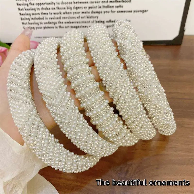 A hand holds five heavy industry light luxury pearl headbands with intricate beadwork and sparkling silver rhinestones