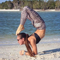 A woman performs a headstand on the beach wearing high waist leopard print leggings and a black strappy sports bra
