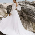 A flowing white wedding dress with long sheer sleeves, high slit, and deep back cut showcasing the back side