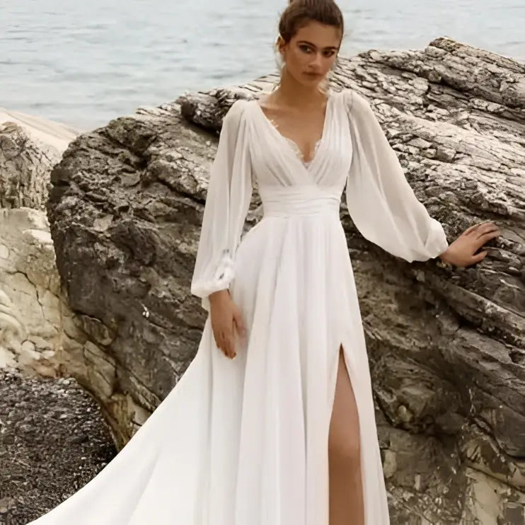 A flowing white wedding dress with long sheer sleeves high slit and elegant long sleeve backless design