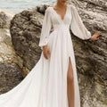 A flowing white wedding dress with long sheer sleeves high slit and elegant long sleeve backless design