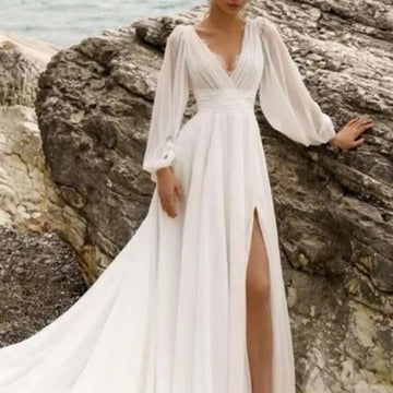 A flowing white wedding dress with long sheer sleeves high slit and elegant long sleeve backless design
