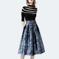 A woman wearing a waist slimming jacquard floral midi skirt in blue with intricate patterns and a black silver top