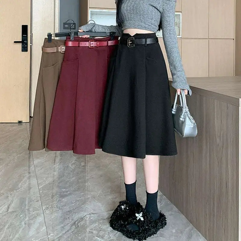 A flared burgundy woolen umbrella skirt with a structured brown high waist and matching belt at mid-thigh length