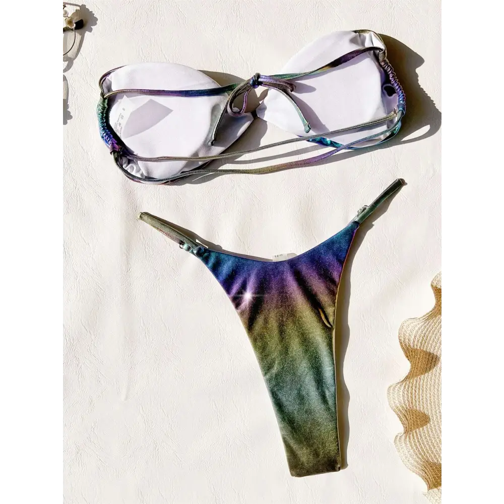 A shimmering iridescent rainbow bikini featuring a gradient swimsuit with purple blue and green hues on thong and bra top