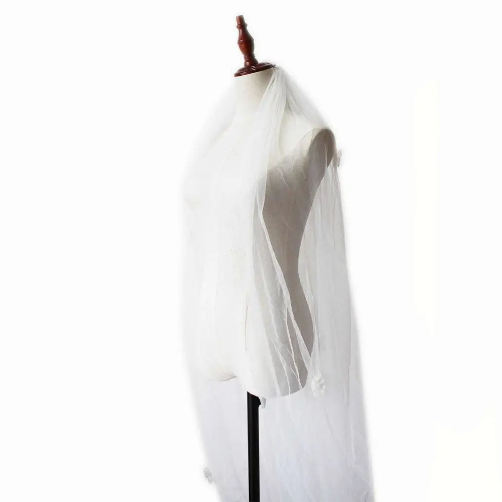 A delicate sheer white tulle veil drapes over a mannequin wearing an ivory lace bridal pearl long tail gown for church wedding