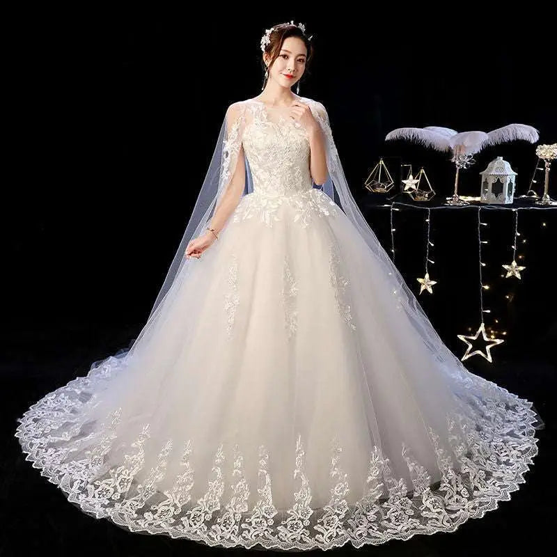 Elegant ivory lace wedding dress with intricate floral embroidery and sheer capelet featuring a flowing tulle skirt