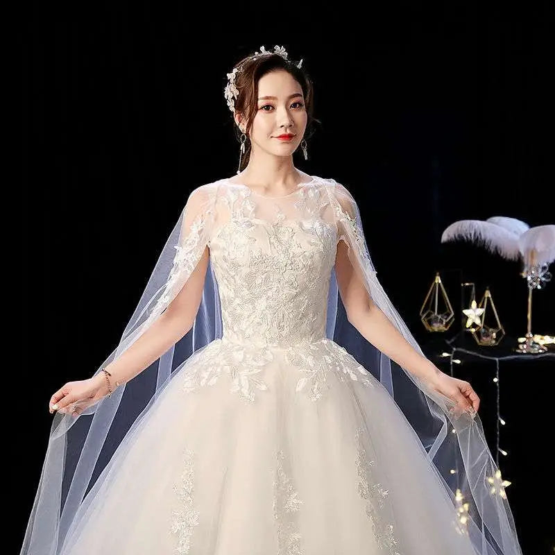 Elegant ivory wedding lace dress featuring intricate lace appliqués and a flowing sheer capelet for brides