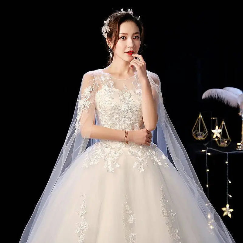 A flowing elegant ivory wedding lace dress with intricate white lace detailing and a sheer capelet