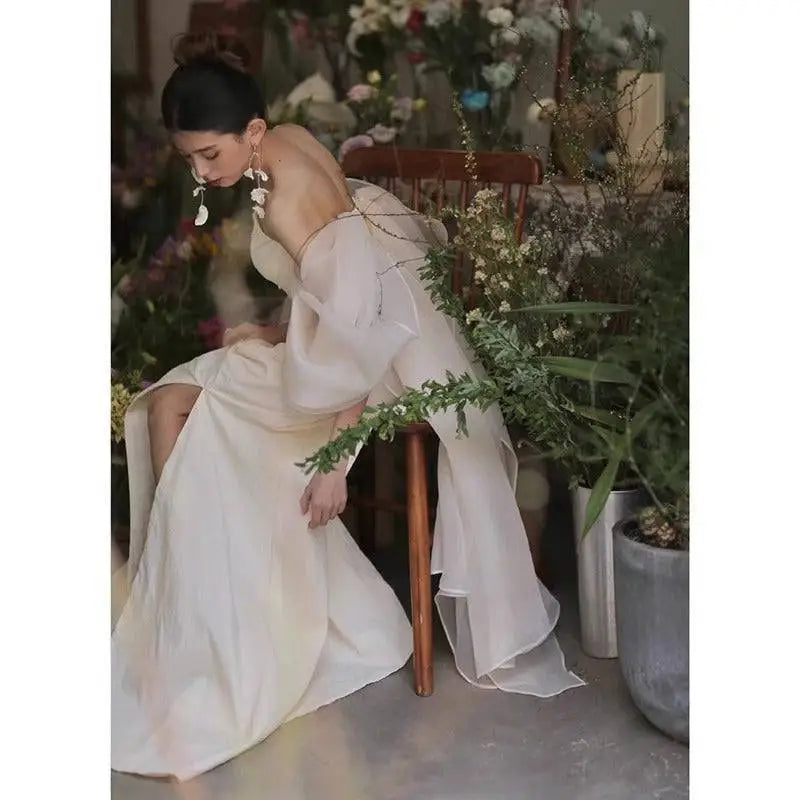 A flowing off-the-shoulder ivory satin outdoor travel shooting light yarn gown with sheer voluminous sleeves and high slit