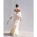 A flowing ivory satin outdoor travel shooting light yarn gown with off-the-shoulder neckline and sheer puffy sleeves