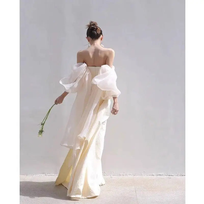 A flowing ivory satin outdoor travel shooting light yarn gown with off-the-shoulder neckline and sheer puffy sleeves